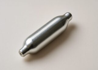 A silver nitrous oxide canister on a neutral background