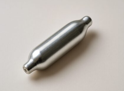A silver nitrous oxide canister on a neutral background