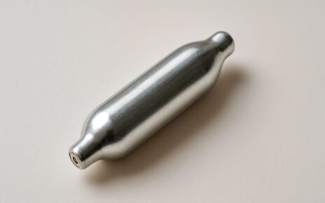 A silver nitrous oxide canister on a neutral background