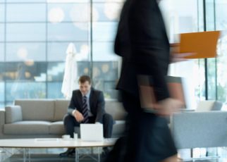 Businessman sitting in modern office lounge using a laptop while colleague walks past, creating dynamic blur. — 5 Proven Mess