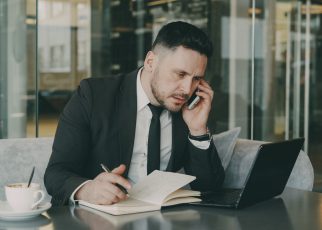 Businessman talks on phone while writing notes in a modern cafe. — Mature Love Made Simple: How Modern Dating Sites Compare f
