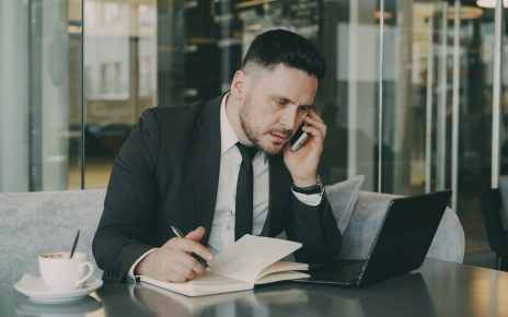 Businessman talks on phone while writing notes in a modern cafe. — Mature Love Made Simple: How Modern Dating Sites Compare f