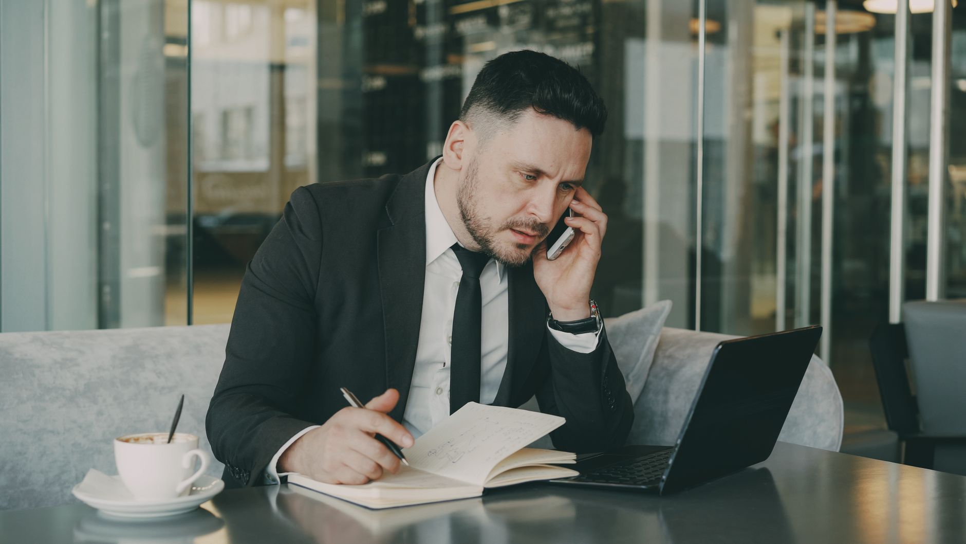 Businessman talks on phone while writing notes in a modern cafe. — Mature Love Made Simple: How Modern Dating Sites Compare f
