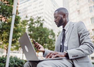 Businessman in a suit using a laptop and smartphone in an urban setting, blending technology with business. — Transform Your
