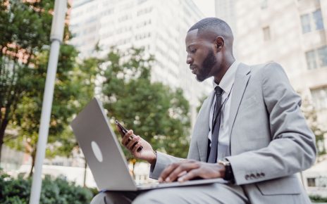 Businessman in a suit using a laptop and smartphone in an urban setting, blending technology with business. — Transform Your
