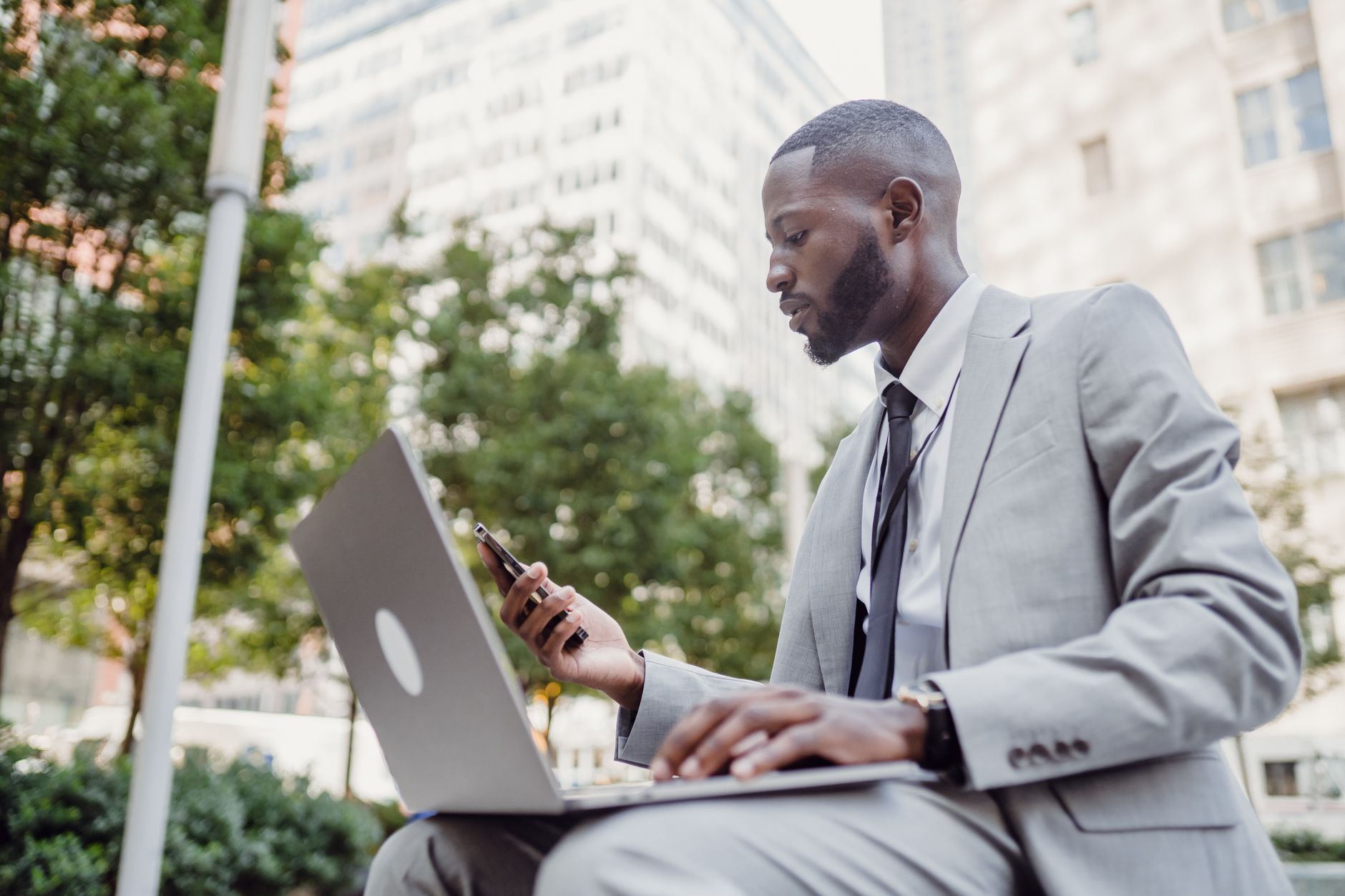 Businessman in a suit using a laptop and smartphone in an urban setting, blending technology with business. — Transform Your