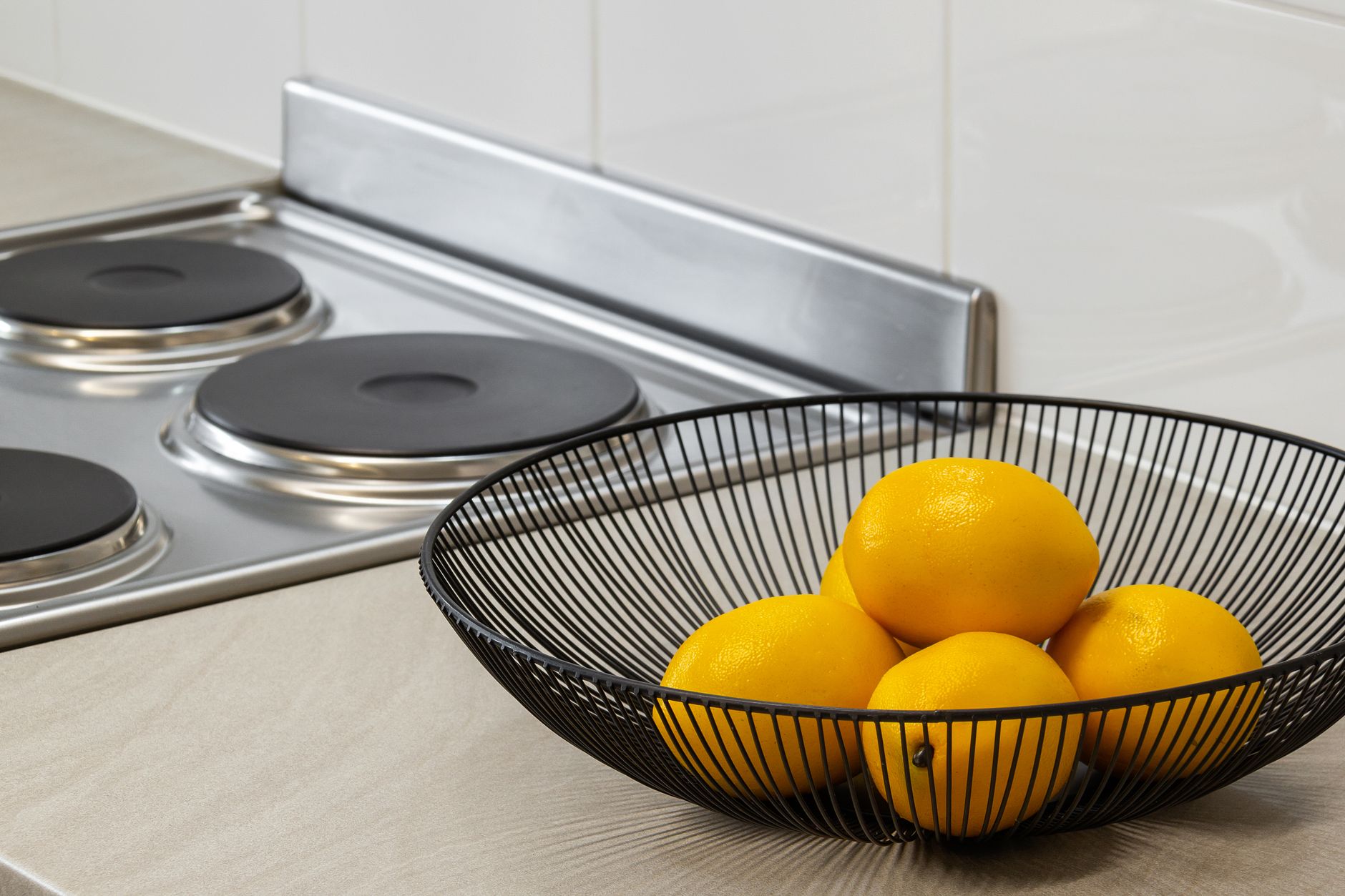 Lemons in a metal bowl on a kitchen counter beside an electric stove, highlighting freshness and simplicity. — Understanding